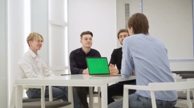 Konsantre genç iş arkadaşları konferans masasında oturmuş yeşil ekranlı dizüstü bilgisayarla konuşuyorlar. Kromakey aygıtı. Meslektaşlar başlangıç aşamasını tartışıyor. İş konsepti.