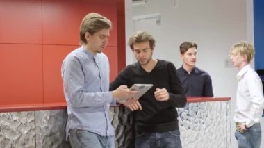 Ofis koridorunda konuşan ve tablet kullanan, arka planda sohbet eden konsantre adamlar. Yeni başlatılan projenin kapalı alanda tartışılacağı konusunda kendinden emin Kafkasyalı milenyumu.