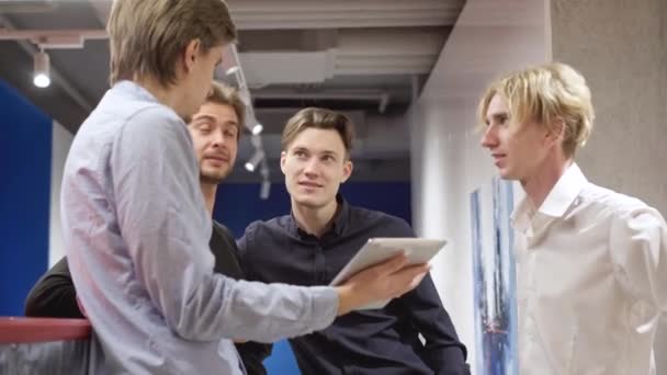 Érdeklődő fiatal kaukázusi férfiak hallgatják, ahogy a kollégájuk elmagyarázza a projektet táblagéppel. Négy magabiztos férfi kolléga áll az irodai folyosón beszélgetni. Üzleti koncepció. — Stock videók