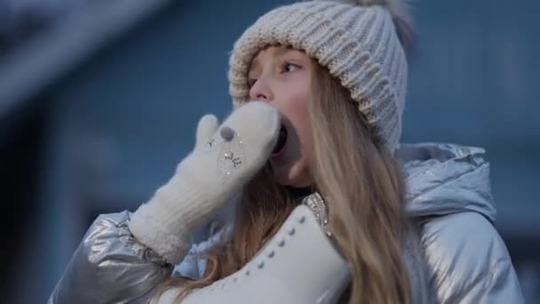 Gyönyörű kaukázusi kislány ásít és mosolyog a jégpályán álló kamerára korcsolyával. Portré bájos gyerek fáradt után téli sport edzés. Életmód-koncepció. — Stock videók