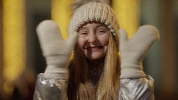 Joyeux charmant fille ouvrant et fermant les yeux avec les mains au ralenti. Portrait d'enfant caucasien joyeux s'amusant en plein air le soir d'hiver de Noël avec des lumières clignotantes à l'arrière-plan. — Video