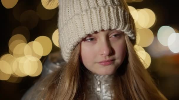 Headshot de charmante fille brune avec les yeux noisette debout à la nuit du Nouvel An en plein air regardant autour. Gros plan de mignon enfant caucasien au crépuscule avec des lumières de Noël à l'arrière-plan. — Video