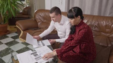 Hamile bir kadının resmi iş kıyafetlerinde konsantre bir adama grafiklerle yardım etmesi. Kafkasyalı hamile kadının evde koltukta oturan kocasını desteklemesi ile meşgul. İş ve hamilelik