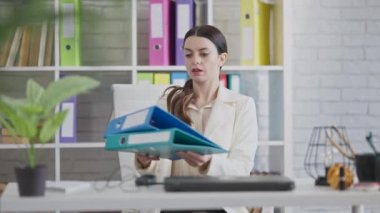 Ofiste oturup dizüstü bilgisayarı yavaş çekimde açan genç ve güzel bir iş kadınının portresi. İş yerinde kapalı mekanda çalışan kendine güvenen, beyaz bir kadın. İş ve başarı.