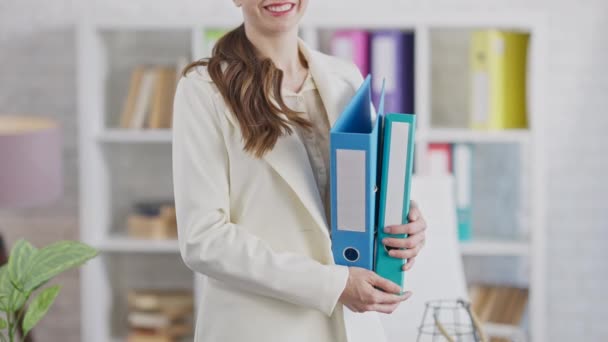 Mujer delgada sonriente irreconocible de pie en la oficina con carpetas de documentos. Hermoso positivo empleado caucásico o CEO posando en el lugar de trabajo. Confianza y negocios. — Vídeos de Stock
