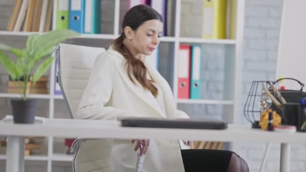 年轻而成功的女人坐在办公室的椅子上，双腿交叉，思维敏捷。瘦小华丽的白种人CEO或在工作场所休息的员工的肖像。女性和商业概念. — 图库视频影像