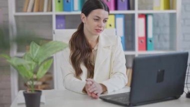 Ofiste otururken bilgisayarında görüntülü konuşma yapan genç, pozitif bir kadın. Kafkasyalı başarılı iş kadınının iş yerinde internette mesajlaşmasının portresi. Kablosuz iletişim kavramı.