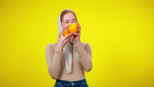 Schlanke, fröhliche rothaarige Frau, die vor gelbem Hintergrund mit Orangen jongliert. Porträt eines lachenden positiven kaukasischen Millennials, der mit gesunden Bio-Früchten posiert und Spaß hat. — Stockvideo