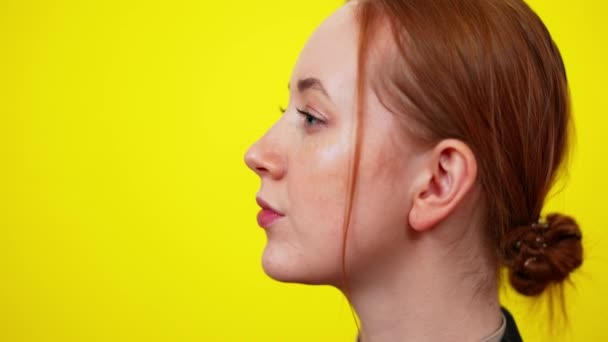 Side view close-up of freckled redhead young woman with green eyes touching chin. Portrait of confident elegant slim Caucasian millennial posing at yellow background. — Stock Video