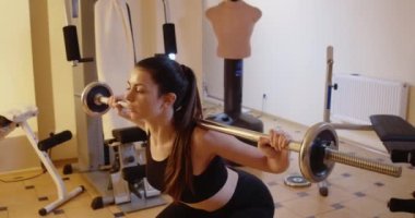 Canlı kamera, halterle çömelmiş ince konsantre kadın hareketini izliyor. Güzel, kendine güvenen beyaz kadın portresi. Spor salonunda. Antrenman konsepti. Sinema 4k ProRes Merkezi.