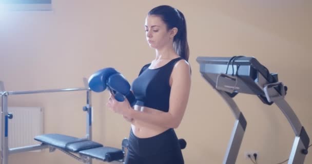 Retrato de tiro medio de una mujer segura y en forma que se pone un guante de boxeo en el gimnasio. Slender magnífico caucásico entrenamiento boxeador femenino en interiores. Autodefensa e igualdad de género. Sede del cine 4k ProRes. — Vídeos de Stock