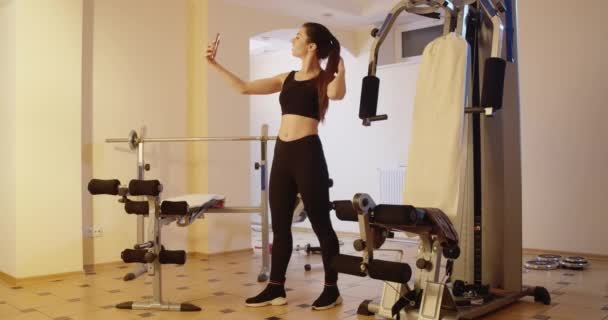 Weitwinkelaufnahme einer schlanken, selbstbewussten Sportlerin, die ein Selfie im Fitnessstudio macht. Glückliche schöne Kaukasierin posiert nach dem Training für Social-Media-Fotos. Millennial lifestyle Cinema 4k ProRes HQ. — Stockvideo