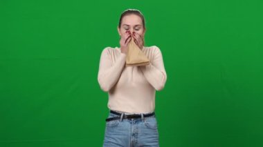 Paniklemiş kadın, yeşil ekrandaki kameraya bakarken kağıt torba içinde nefes alıyor. Korkmuş beyaz bir kadının portresi. Sakinleşiyor ve nefes veriyor. Kromakey.