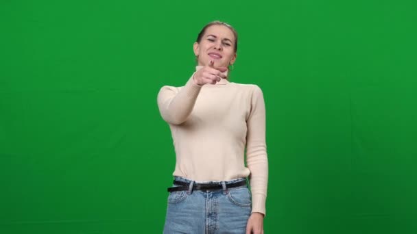 Een vrouw die naar de camera wijst en lacht. portret van jonge onbeschofte slanke blanke dame op groen scherm. Pesten op chromakey achtergrond. — Stockvideo