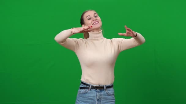 Mujer con sonrisa dentada en auriculares imitando el vals en la pantalla verde. Retrato de dama feliz y confiada bailando en el fondo cromakey. Concepto de danza clásica. — Vídeo de stock
