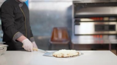 Covid-19 maskeli aşçı ve eldivenler mutfakta pizza hamuru pişirme ve kapama fırını koyuyor. Profesyonel bir aşçının portresi restoranda Coronavirüs salgınıyla ilgili yemek hazırlıyor..