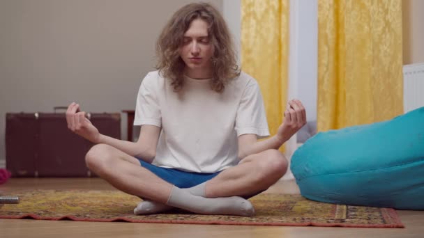 Jonge tachtiger jaren gestileerde man mediterend in lotus poseren thuis. Portret van een ontspannen blanke die yoga beoefent in de jaren '90. Meditatie en sport in retro stijl. — Stockvideo