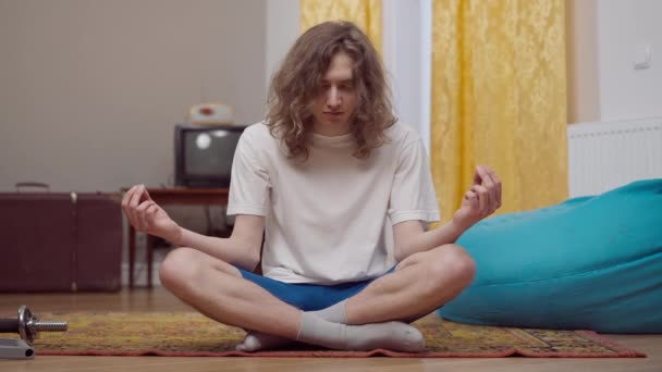 Portret van kalme jonge retro man met lang krullend haar die in slaap valt zittend in lotus poseren binnen. Een man uit de jaren negentig die thuis yoga oefent. Yogi mediteren in de jaren tachtig. — Stockvideo