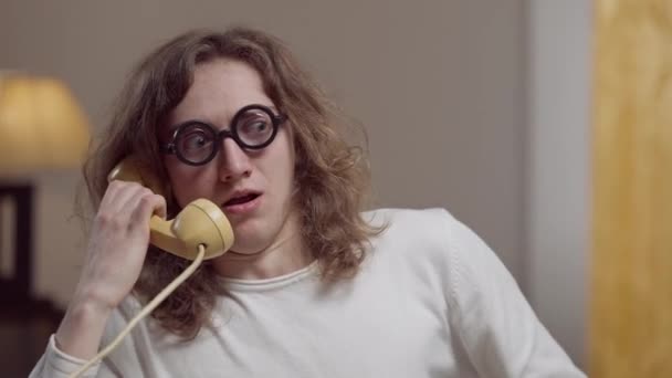 Portret van een geniale nerd in een retro bril die binnen praat op een vintage telefoon. Slimme blanke student of werknemer in de jaren tachtig of negentig thuis. Levensstijl en intelligentie concept. — Stockvideo