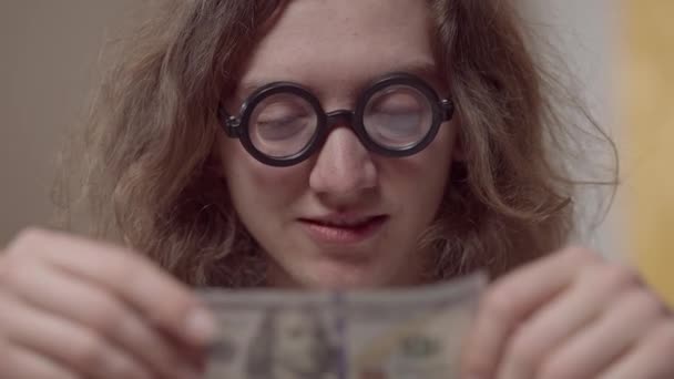 Een foto van een gelukkige man in een bril die glimlachend naar dollars kijkt. Close-up portret van Kaukasische nerd met contant geld in de jaren tachtig of negentig. Succes en rijkdom concept. — Stockvideo