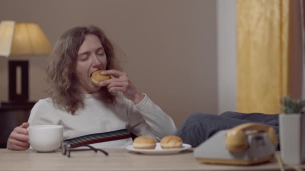 무료 역학자는 도넛을 먹고 차나 커피를 마시며 실내 테이블에 발을 올려 놓고 앉아 있다. 1990 년 대에 집에서 쉬고 있는 행복 한 백인 남자의 초상화. 여가 와 생활 방식. — 비디오