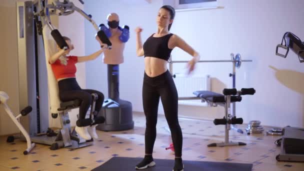 Portrait large de la jeune femme blanche en forme confiante faisant des exercices de sport flexion comme entraînement millénaire sur l'équipement de remise en forme en arrière-plan. Slim belles femmes faisant de l'exercice en salle de gym à l'intérieur. — Video