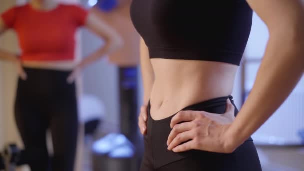 Gros plan ventre de mince jeune femme caucasienne respirant et expirant muscles d'entraînement avec flou entraîneur méconnaissable en arrière-plan. Sportive mince travaillant dans la salle de gym à l'intérieur. — Video