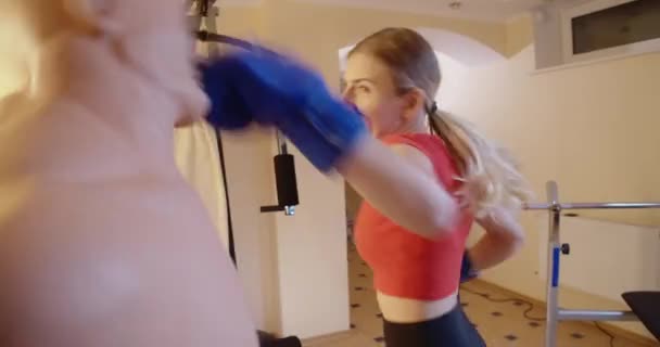 Joven mujer deportiva enojada golpeando maniquí en el gimnasio en el interior. Retrato de la furiosa deportista caucásica haciendo ejercicio. Control de ira y concepto de artes marciales. Sede del cine 4k ProRes. — Vídeo de stock