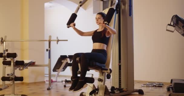 Brett fotograferat porträtt av fokuserade idrottskvinnor som tränar handmusklerna på träningsmaskinen i gymmet. Koncentrerad vacker smal vit kvinna som motionerar inomhus. Bio 4k ProRes HQ. — Stockvideo