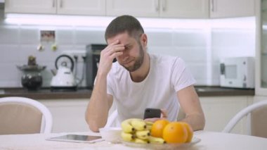 Stresli, yakışıklı, beyaz bir adam. Düşünüyor ve elini tutuyor. Mutfakta oturuyor. İçeride sorun yaşayan endişeli bir adamın portresi. Endişe ve stres kavramı.