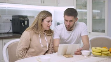 Kafkas erkek ve kadın internette tablet üzerinde sörf yapıyor. Evdeki mutfakta oturuyor. Heyecanlı, mutlu, gülümseyen, sarılan beyaz bir eş. Neşe ve mutluluk kavramı.