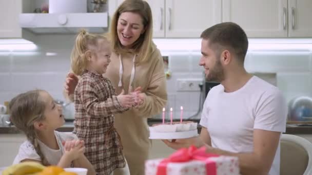快乐的高加索家庭祝贺女婴三周岁生日。快乐的母亲、父亲和女儿用蜡烛拍手叫好，笑着拿着蛋糕。慢动作. — 图库视频影像