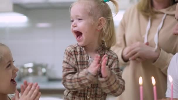 Retrato de bebê animado menina batendo palmas e rindo soprando velas no bolo de aniversário. Feliz filha caucasiana comemorando férias com a família em kicthen em casa. — Vídeo de Stock