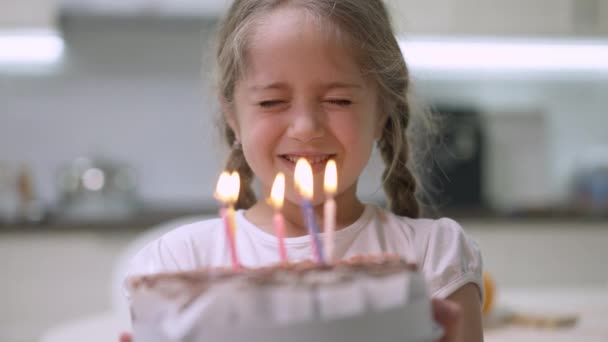Közelkép egy bájos kislányról csukott szemmel, aki kívánságot teljesít és gyertyákat fúj a szülinapi tortán. Egy boldog kaukázusi csinos gyerek portréja, aki otthon ünnepli a születésnapját. Öröm és életmód. — Stock videók