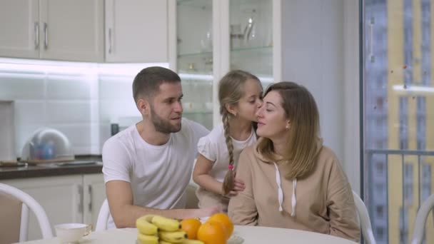 Gelukkig Kaukasische dochter zoenen en knuffelen ouders kijken naar de camera en glimlachen. Portret van een vreugdevolle ontspannen familie die samen genieten van de vrije tijd in het weekend thuis. Vreugde en levensstijl. — Stockvideo