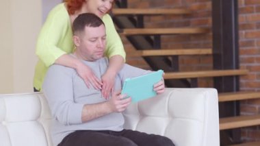 Neşeli bir eş, özümsenmiş kocasını kucaklıyor, tablette internette sörf yapıyor. Beyaz bir kadının yakışıklı, rahat bir adamı kucaklayıp evdeki kanepede oturması. Aile eğlencesi..
