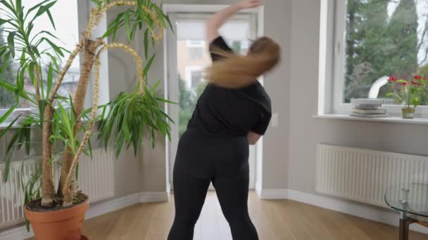 Vista posterior de la mujer caucásica con sobrepeso motivado doblando el calentamiento de los entrenamientos en interiores. Deportista persistente de talla grande haciendo ejercicio en casa por la mañana. Autoestima y auto-mejora. — Vídeos de Stock