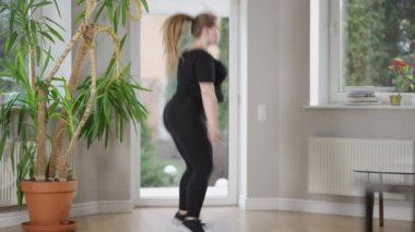 İçerde zıplayan kilolu sporcu kadının yan görüntüsü. Kendine güvenen beyaz bir genç kadının evde antrenman yapması. Fitness ve sağlıklı yaşam tarzı konsepti.