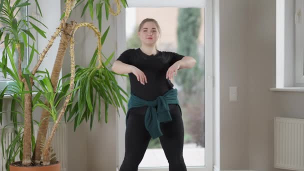 Portret van een mollige jonge vrouw die binnenshuis borstcirkels opwarmt. Zelfverzekerde positieve plus-size dame training thuis in de ochtend. Fitness en gezond lifestyle concept. — Stockvideo