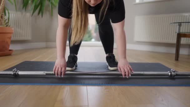 Gordinha caucasiano jovem mulher levantando barbell de pé no tapete de exercício em casa. Pernas de esportista motivado concentrado exercitando treinamento dentro de casa. Conceito de treino e desporto. — Vídeo de Stock