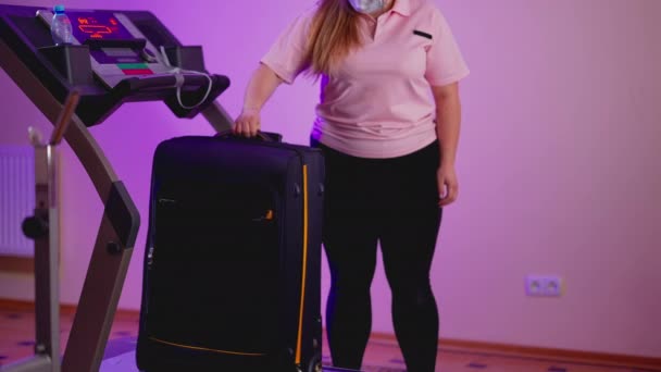 Jeune femme méconnaissable en masque facial Covid utilisant tapis roulant comme bande transporteuse. Millénaire taille plus imitant salon de départ de l'aéroport dans la salle de gym à domicile à l'intérieur. Coronavirus concept de tourisme. — Video