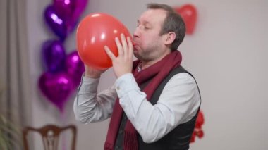 Esmer adam sevgililer gününde kalp şeklinde balon şişirip evden çıkıyor. Romantik beyaz bir koca ya da erkek arkadaşın evde partnerine hazırladığı sürpriz portresi..