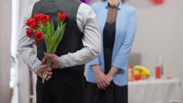 Rückansicht des nervösen erwachsenen kaukasischen Mannes, der einen Strauß Tulpen zum Valentinstag für eine verschwommene Frau hält, die im Hintergrund wartet. Ängstlich liebender Freund überrascht Freundin im Urlaub mit Blumen. — Stockvideo