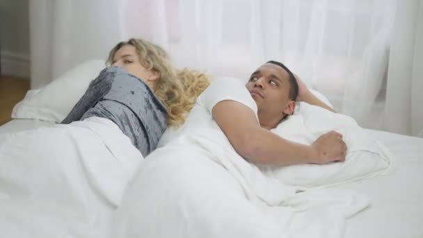 Argued interracial jeune couple couché dans le lit dos à dos. Triste homme afro-américain et femme caucasienne regardant par-dessus l'épaule se détourner. Difficultés relationnelles et concept de conflit — Video