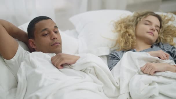 Jeune petit ami heureux admirant petite amie endormie et regardant la caméra souriant. Portrait d'un homme afro-américain amoureux couché au lit avec une femme blanche. Concept de loisirs et d'amour. — Video