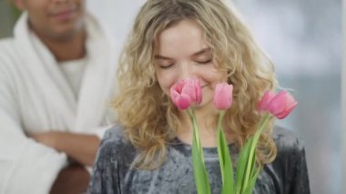 Çekici, mutlu, genç, zayıf bir kadının portresi. Arka planda tanınmayan bir adamla birlikte güzel pembe laleler kokusu. Sabah erkek arkadaşından hediye almış tatmin olmuş bir kız arkadaş..