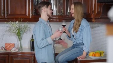 Kaygısız genç kadın mutfak tezgahında oturan yakışıklı adam kadeh kaldırıyor. Mutlu gülen beyaz çift gülümseyen gözlüklerden kırmızı şarap içiyor. Eğlence ve eğlence..