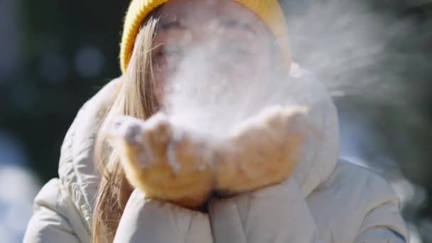 Close-up lachend gezicht van jonge charmante vrouw die sneeuw blaast van gele wanten. Headshot portret van blij opgewonden vreugdevolle toerist genieten van de winter weer buiten poseren. — Stockvideo