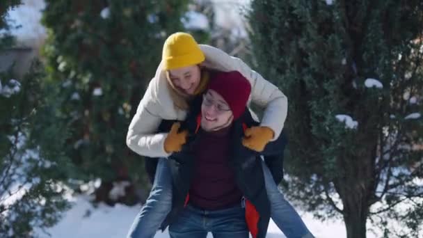 Fröhliche Freundin springt ihrem Freund auf den Rücken und posiert an einem sonnigen Wintertag im Freien. Glückliches kaukasisches Millennial-Paar, das aktive Reisen im Nordwald genießt. Bindung und Tourismus. — Stockvideo