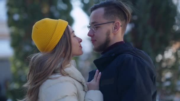 Vista lateral de pareja cariñosa frotando narices sonriendo girando hacia la cámara. Retrato de feliz joven caucásico millennial hombre y mujer disfrutando del ocio juntos en el día de invierno al aire libre posando. — Vídeos de Stock